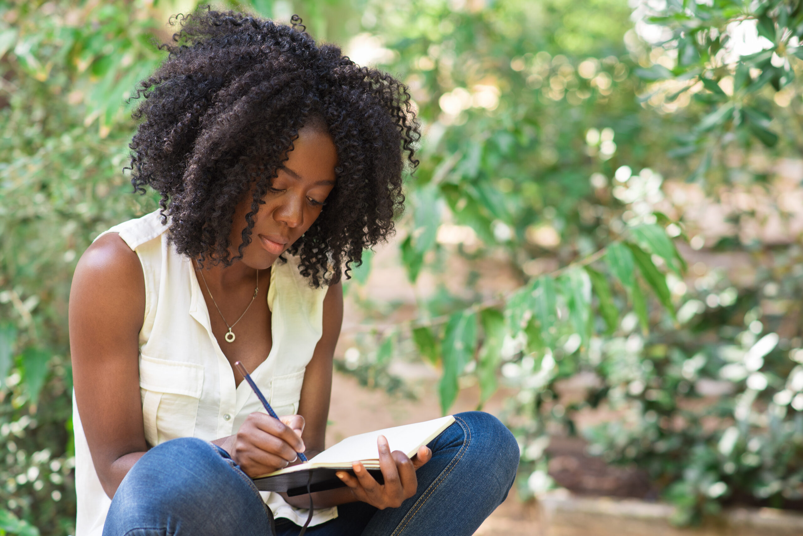 A woman overcoming writer's block and procrastination by starting her book writing journey in a serene natural setting with a notebook and pen.